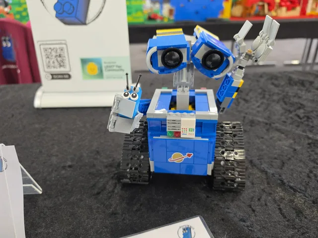A small blue robot built from LEGO bricks with large eyes, beside the Bricks am Meer mascot